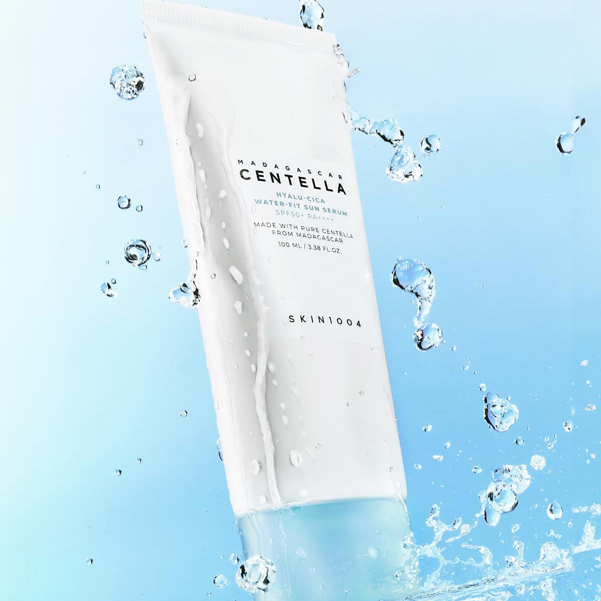 SKIN1004 Madagascar Centella Hyaluronic Acid Water-Fit Sun Serum 100ml, bouteille blanche sur fond bleu avec éclaboussures d'eau.