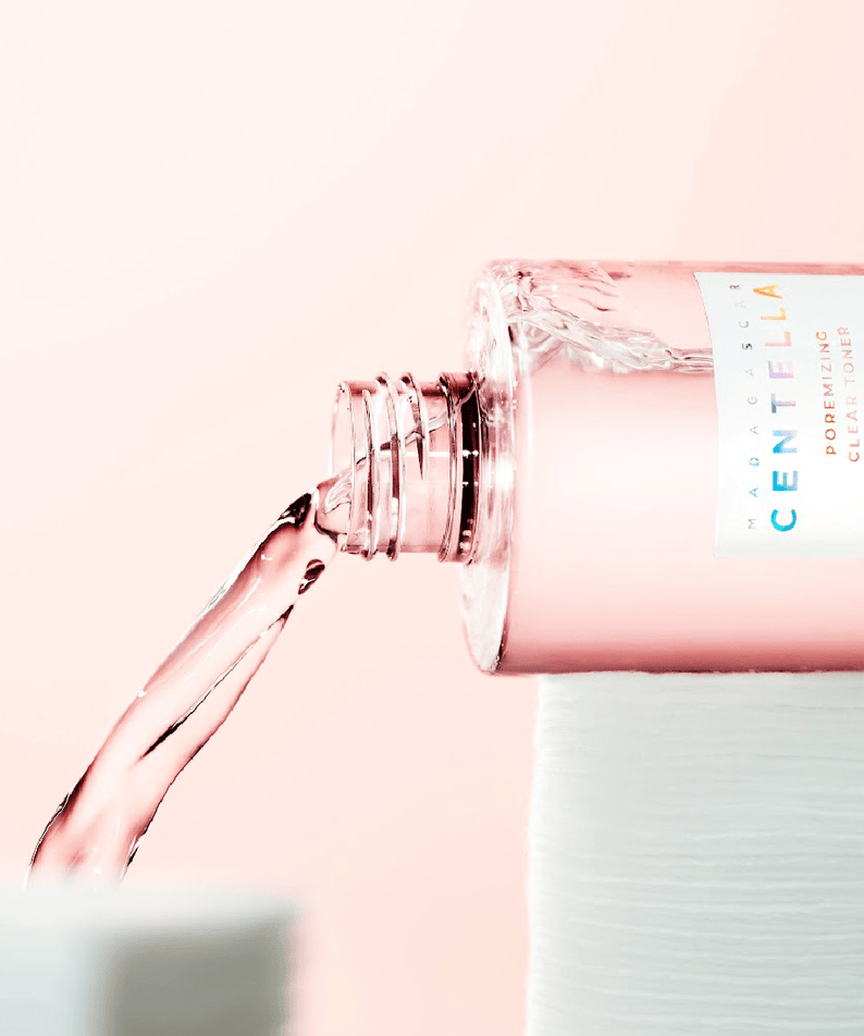 SKIN1004 Madagascar Centella Poremizing Clear Toner 210ml, flacon rose et mains vers le spray, contexte beauté.