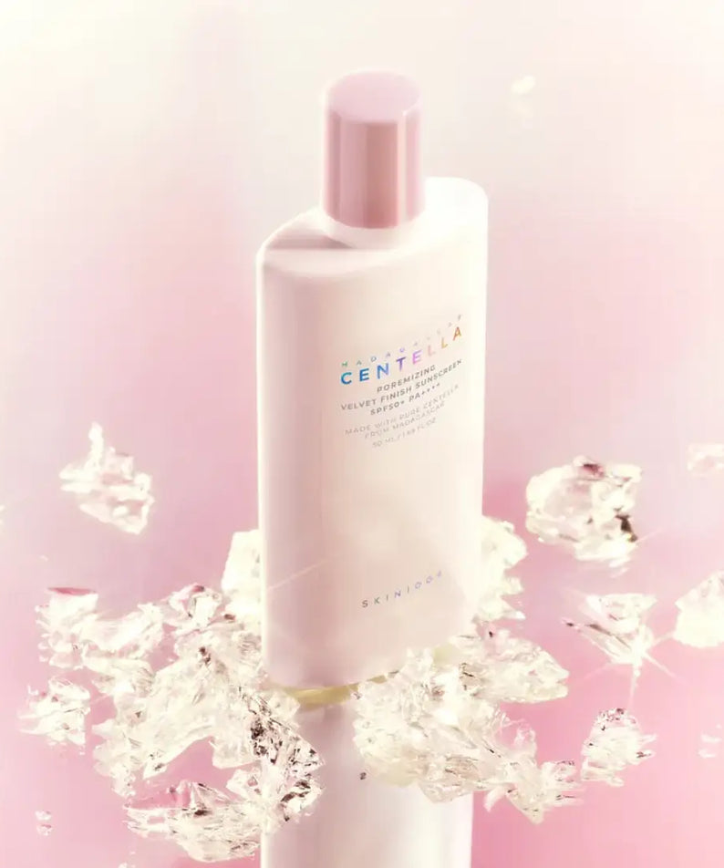 SKIN1004 Madagascar Centella Poremizing Velvet Finish Sunscreen 50ml, flacon crème visage, marque SKIN1004, fond rose avec éclaboussures.