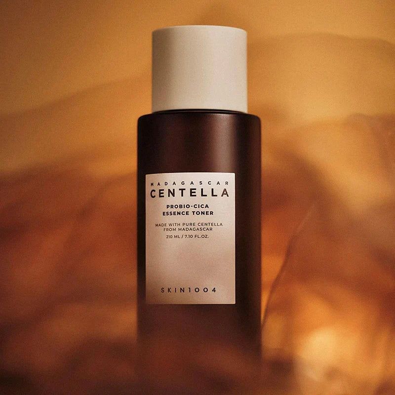 SKIN1004 Madagascar Centella Probio-cica Essence Toner 210ml, flacon noir sur fond beige chaud, présentation produit SKIN1004.