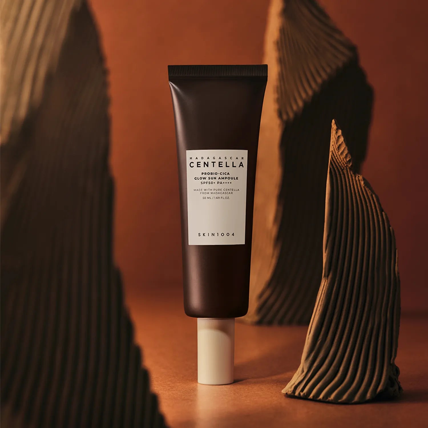 SKIN1004 Madagascar Centella Probio-cica Glow Sun Ampoule 50ml, marque SKIN1004, tube au centre sur fond chaud, esthétique skincare