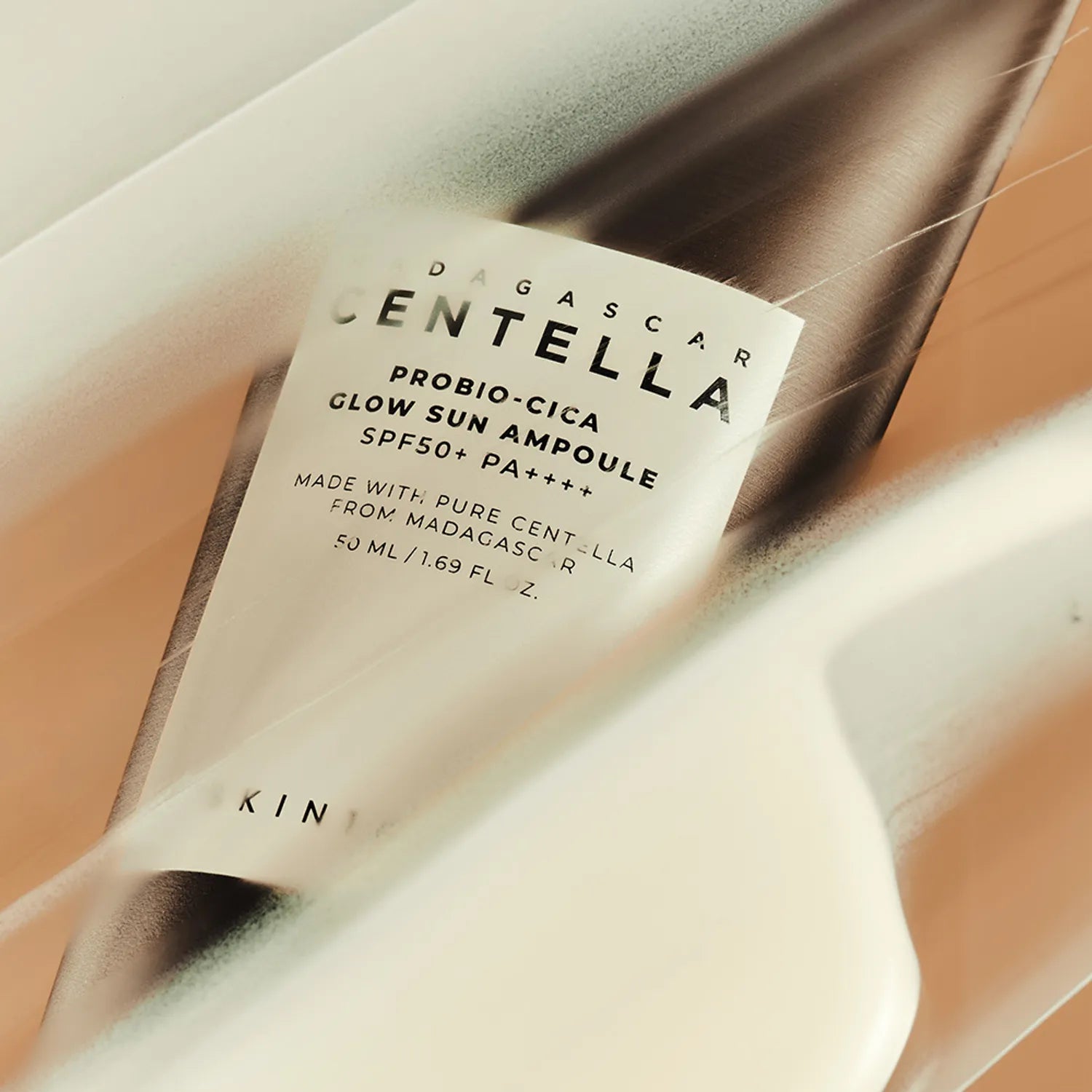 Décris l'image en français : SKIN1004 Madagascar Centella Probio-cica Glow Sun Ampoule 50ml, flacon sur fond beige, marque affichée