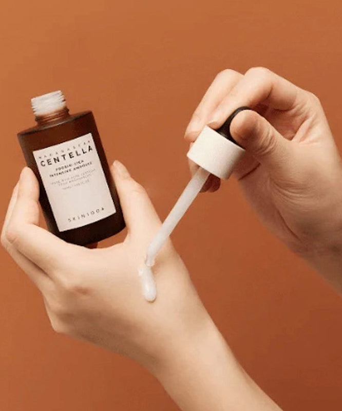 SKIN1004 Madagascar Centella Probio-cica Intensive Ampoule 50ml, marque SKIN1004, mains appliquant l’ampoule sur fond orange, texture fluide