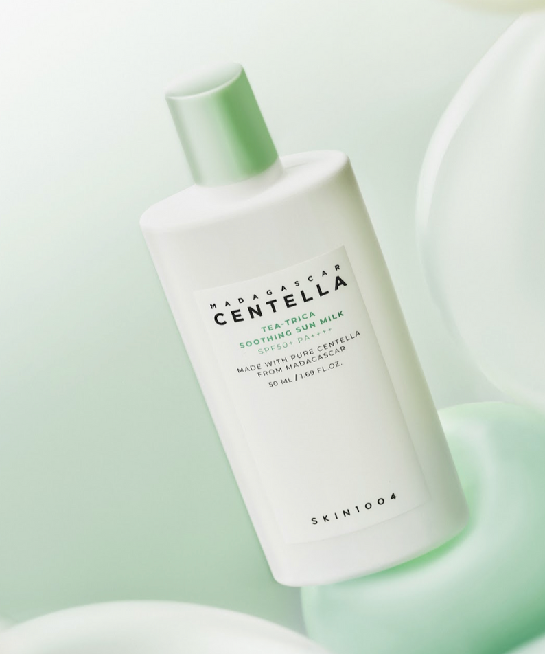 Décris l'image en français : SKIN1004 Madagascar Centella Tea-trica Soothing Sun Milk 50ml de SKIN1004, flacon blanc vert sur fond pastel.