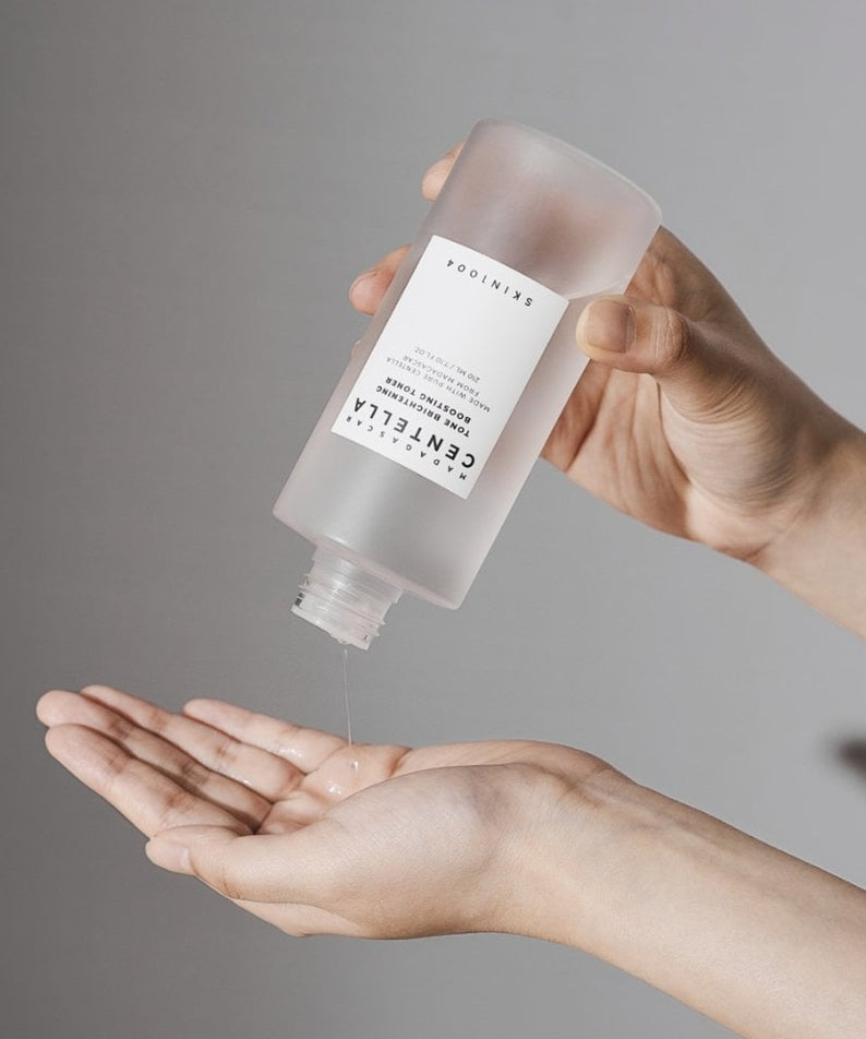 SKIN1004 Madagascar Centella Tone Brightening Boosting Toner 210ml : main applique le toner, marque SKIN1004, fond gris, gouttes