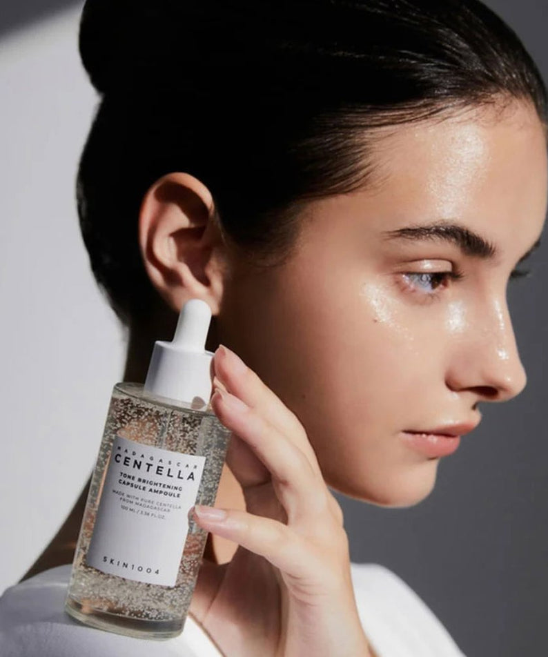 SKIN1004 Madagascar Centella Tone Brightening Capsule Ampoule 100ml, flacon sur peau lumineuse, femme appliquant le sérum, fond blanc