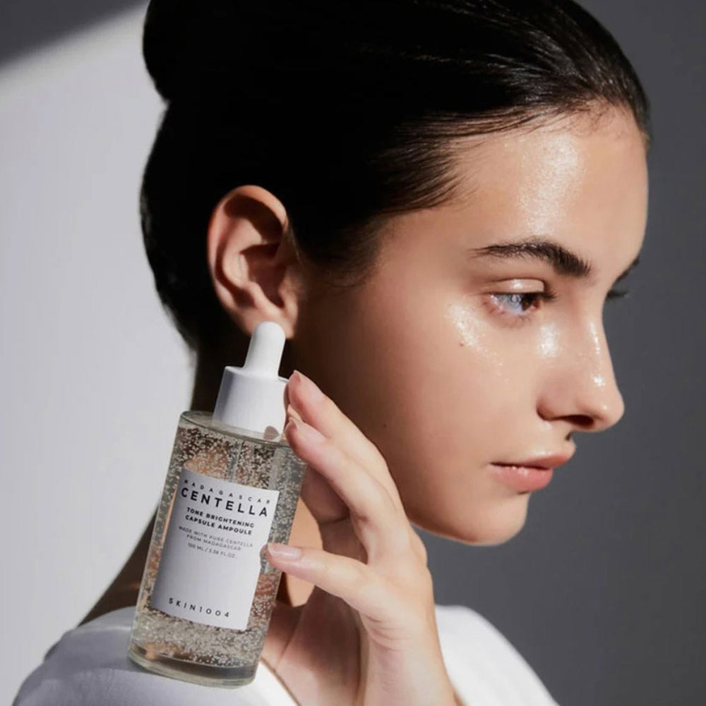 SKIN1004 Madagascar Centella Tone Brightening Capsule Ampoule 100ml, flacon sur peau lumineuse, femme appliquant le sérum, fond blanc