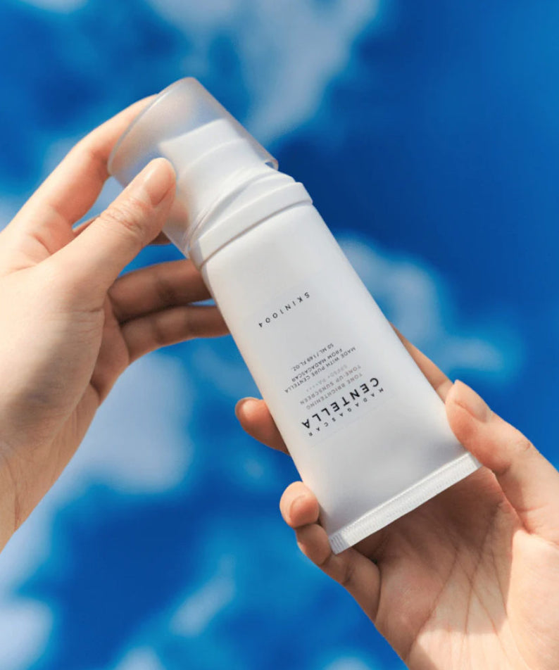 SKIN1004 Madagascar Centella Tone Brightening Tone-Up Sunscreen 50ml de la marque SKIN1004, tube tenu sur fond bleu.