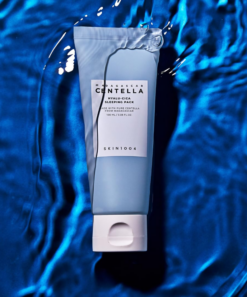 La crème hydratante SKIN1004 Madagascar Centella Hyalu-Cica Acid Sleeping Pack 100ml posée sur un arrière-plan bleu aquatique.