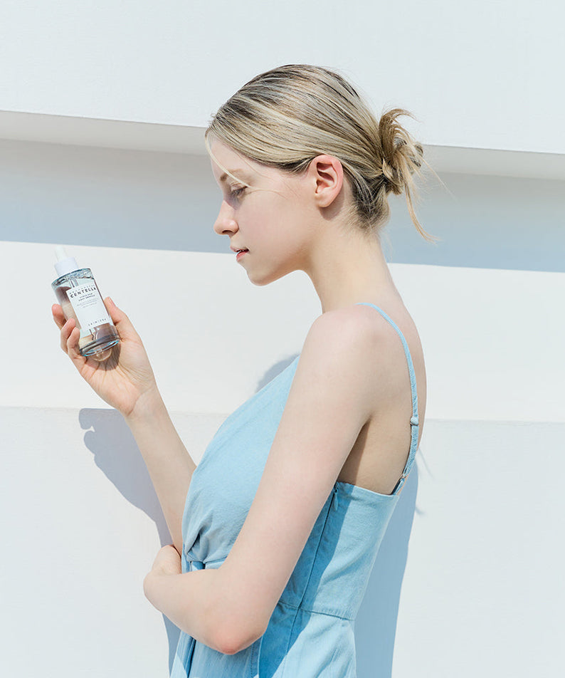 Femme tenant un flacon de SKIN1004 Madagascar Centella Hyalu-Cica First Ampoule 100ml contre un fond blanc.