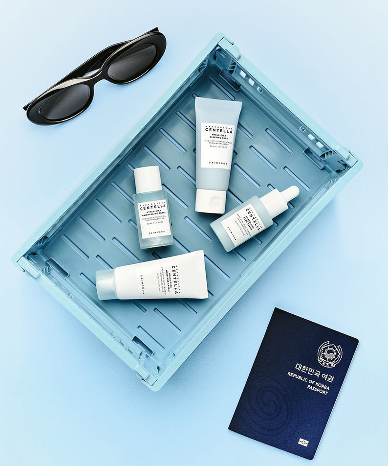 Kit de voyage SKIN1004 Madagascar Centella Hyaluronic Acid avec lunettes et passeport, présentation élégante sur fond bleu.
