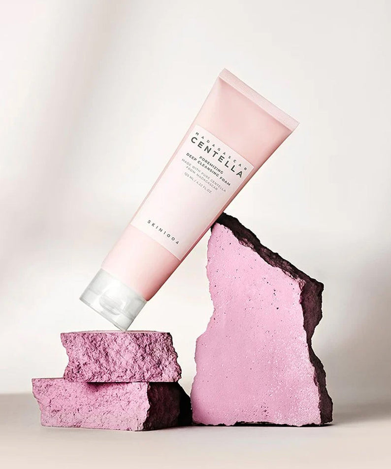 SKIN1004 Madagascar Centella Poremizing Deep Cleansing Foam 125ml en mise en scène artistique avec fond texturé rose.