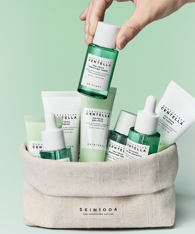 Trousse de voyage SKIN1004 Madagascar Centella Teatrica comprenant diverses bouteilles et tubes de soins de la peau sur fond vert.