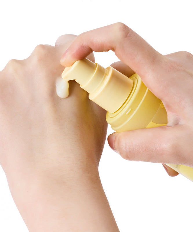 SKINFOOD Banana PDRN Booster Serum 80ml de la marque SKINFOOD, mains tenant le flacon jaune sur fond blanc.