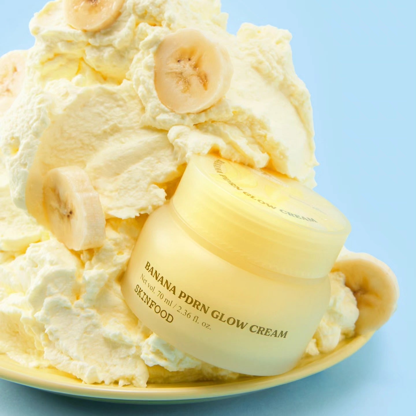 SKINFOOD Banana PDRN Glow Cream 70ml, crème lissante sur fond bleu avec banane et texture crémeuse, photo produit.