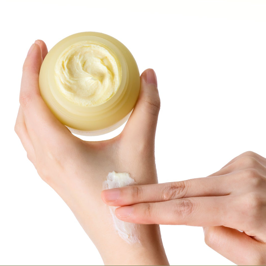 SKINFOOD Banana PDRN Glow Cream 70ml, pot de crème cosmétique jaune, texture sur les mains, studio blanc.
