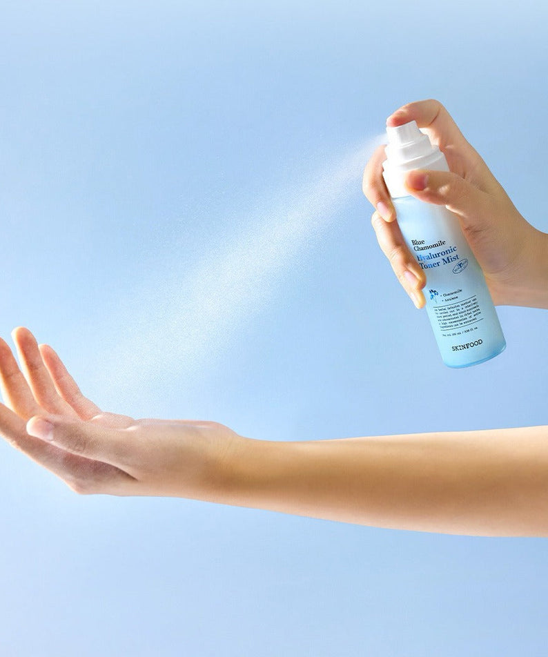 SKINFOOD Blue Chamomile Hyaluronic Toner Mist 100ml, brume visage d'une main sur bras, fond bleu, soin hydratant