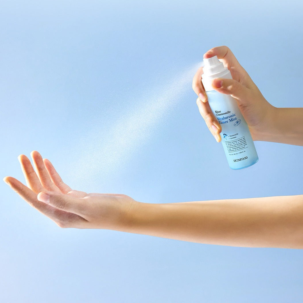 SKINFOOD Blue Chamomile Hyaluronic Toner Mist 100ml, brume visage d'une main sur bras, fond bleu, soin hydratant