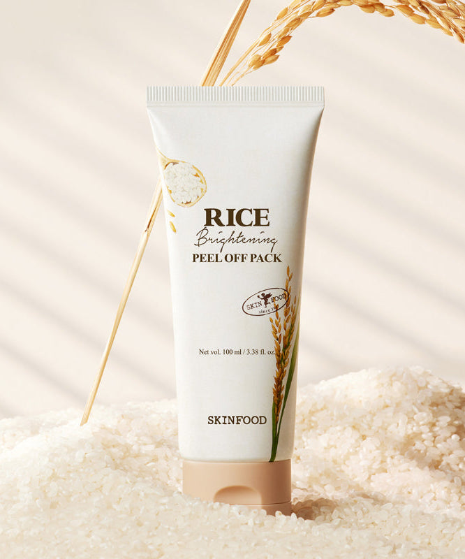 SKINFOOD [NEW] Rice Brightening Peel-Off Pack 100ml, tube crème sur fond beige avec grains de riz et ruban doré