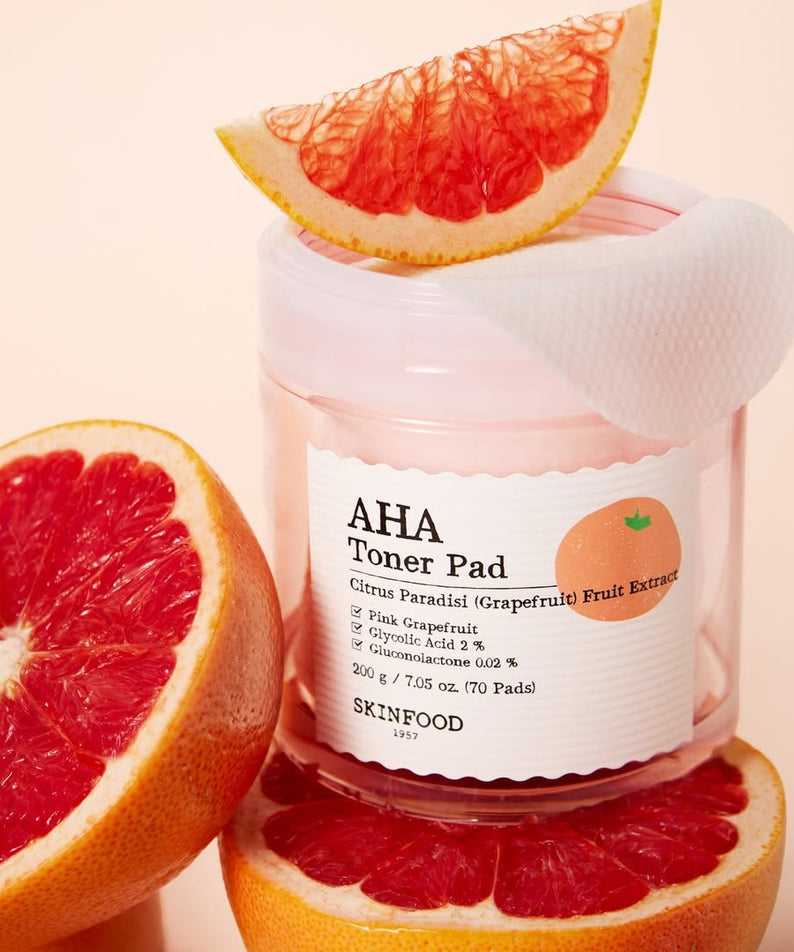 SKINFOOD Pink Grapefruit AHA Toner Pad 70 sheets, flacon et pads à côté de pamplemousse, contexte visuel beauté
