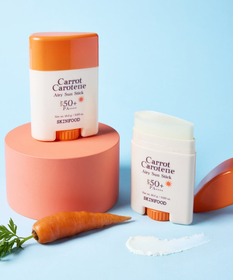 Photo du SKINFOOD Carrot Airy Soft Sun Stick 18.5g avec carotte et crème blanche sur fond bleu.