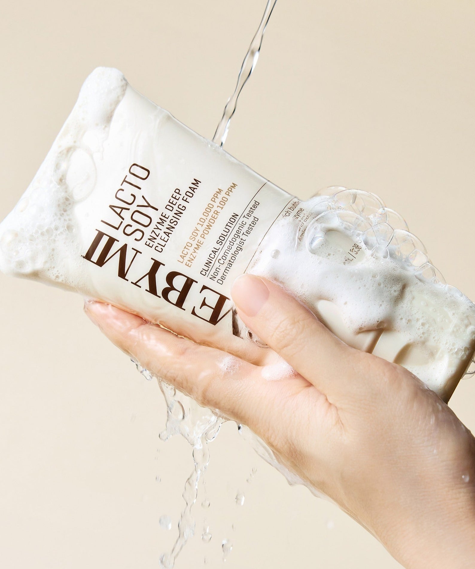 Produit SOME BY MI Lactosoy Enzyme Deep Cleansing Foam 100ml tenu avec mousse sur fond beige, lavage efficace visage.