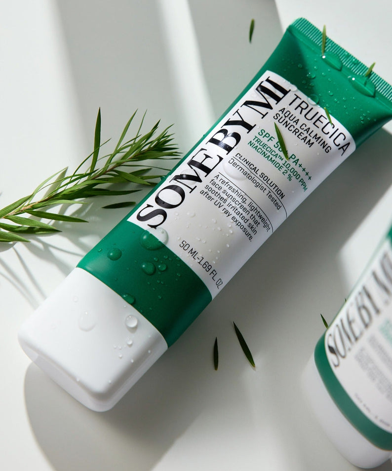 Crème solaire SOME BY MI Truecica Aqua Calming Sun Cream 50ml sur fond blanc, avec gouttelettes d'eau et feuillage.