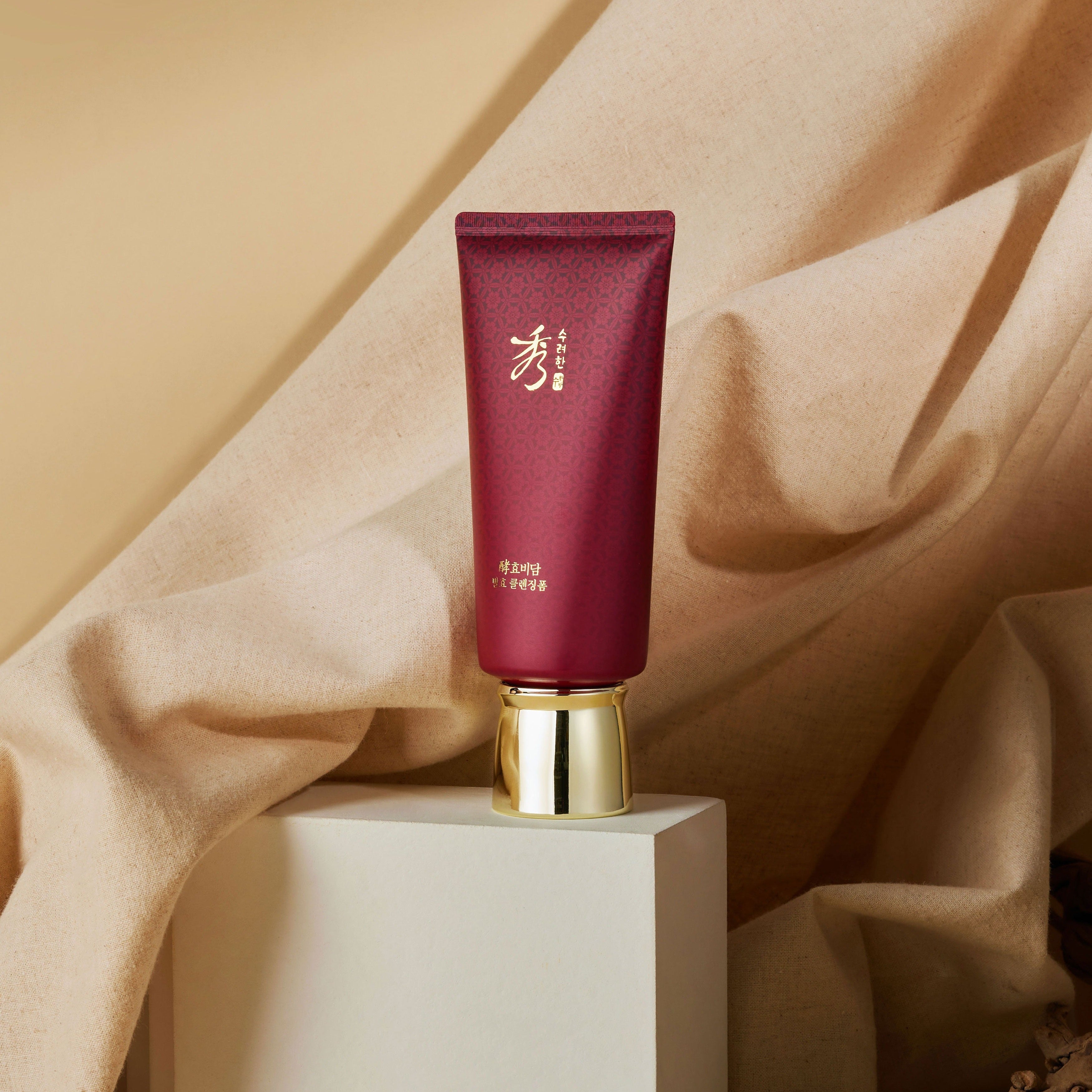 SOORYEHAN Hyobidam Fermented Cleansing Foam 160ml sur podium, flacon rouge bordeaux, tissu beige en arrière-plan.