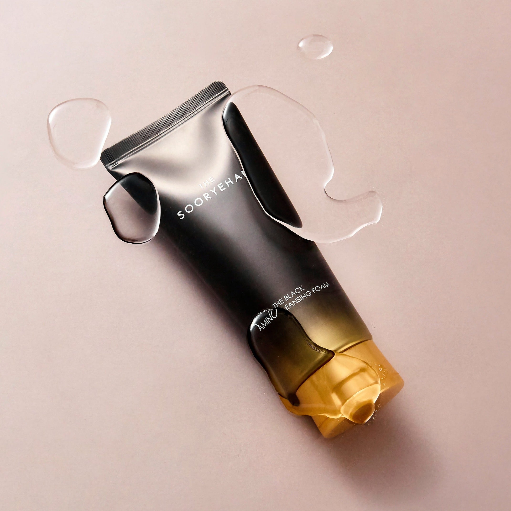 SOORYEHAN The Black Amino Cleansing Foam 150ml, marque SOORYEHAN, flacon noir sur fond beige avec gouttes d'eau.