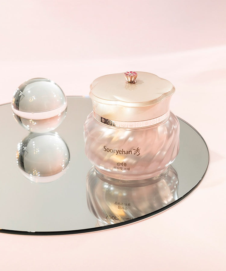 Crème "SOORYEHAN Ultimate Cream 50ml" posée sur un miroir, emballage élégant et perle brillante à côté, cosmétique haut de gamme.