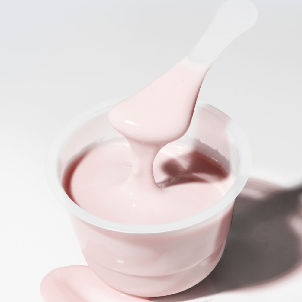 Décris l'image en français: SUNGBOON EDITOR Boosting Modeling Pack Apple Peel Glow Soothing, crème rose en pot, texture sur spatule.