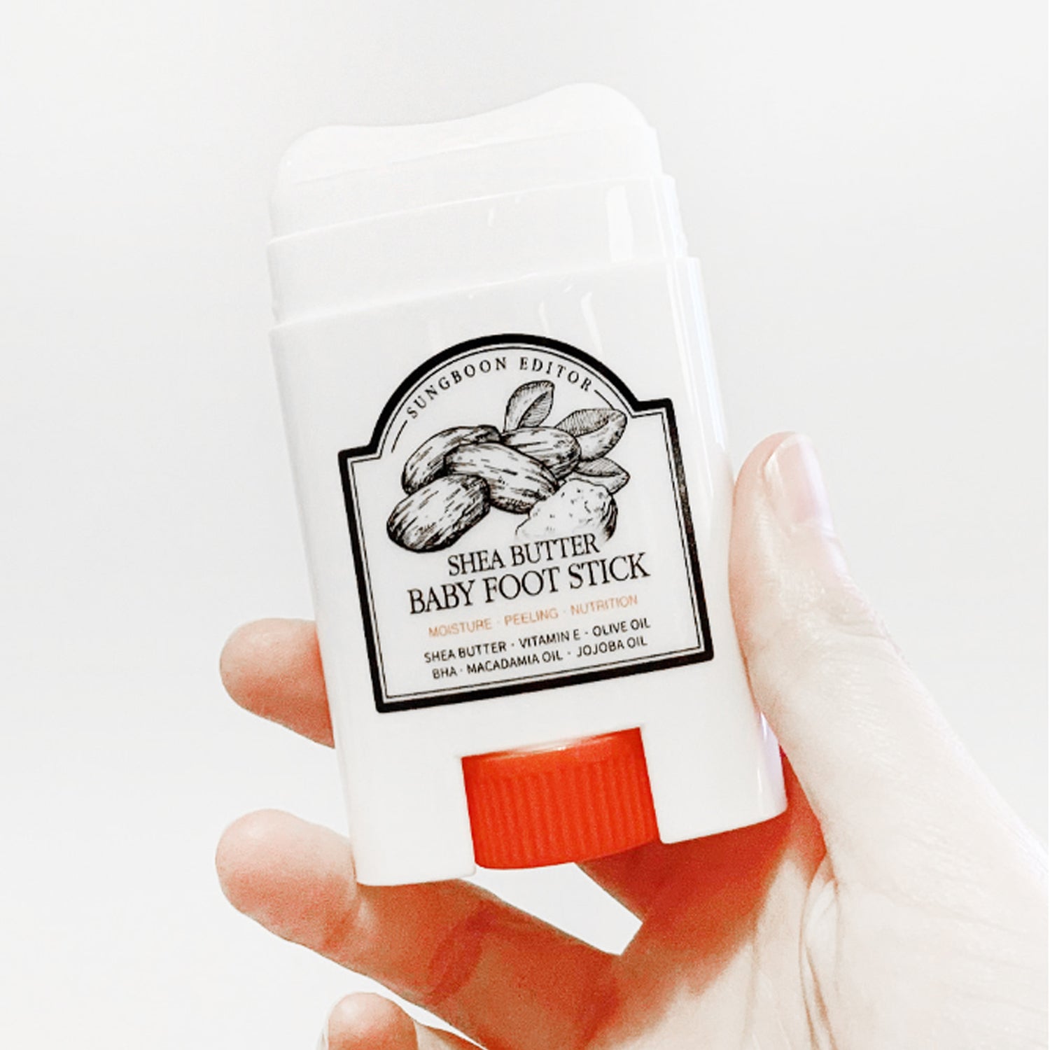 SUNGBOON EDITOR Shea Butter Baby Foot Stick : stick au beurre de karité, main tenant le produit sur fond blanc.