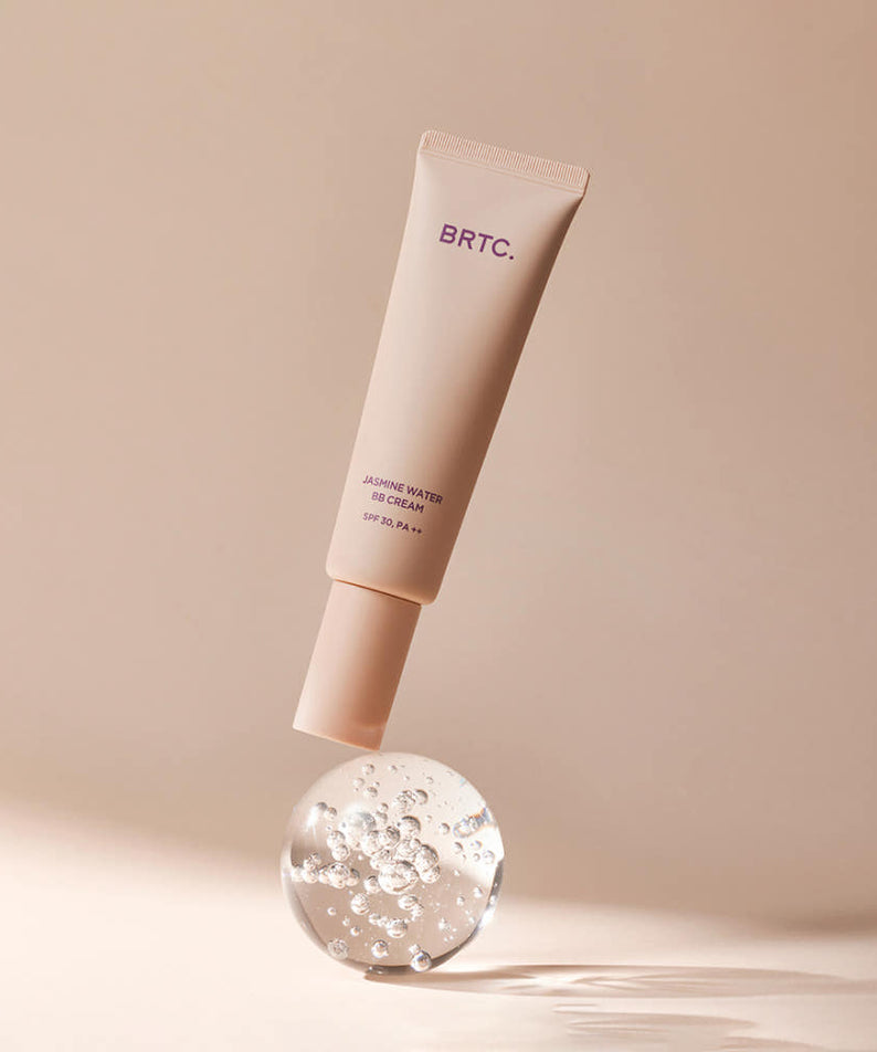 BRTC Jasmine Water BB Cream 60g de la marque BRTC, tube beige sur fond beige avec gouttes de texture, studio maquillage