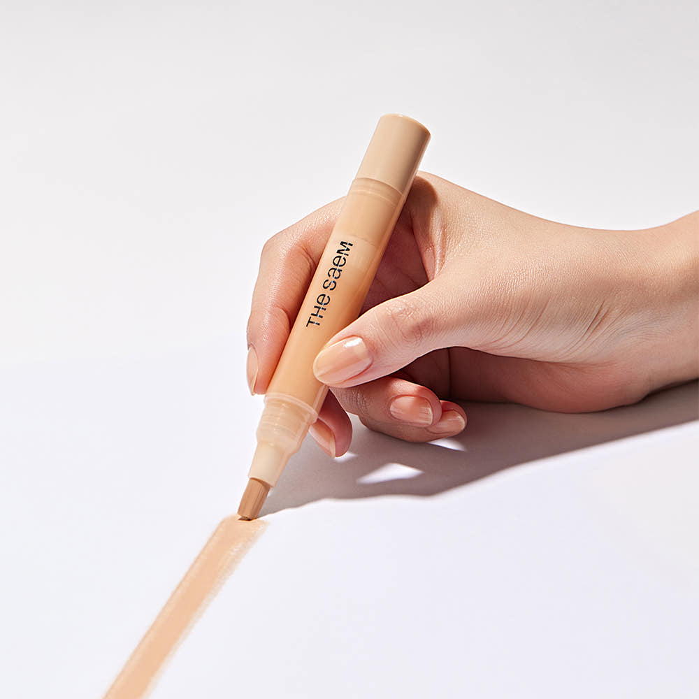 THE SAEM Cover Perfection Pen Concealer : main tient le stylo correcteur maquillage, fond blanc, marque THE SAEM.