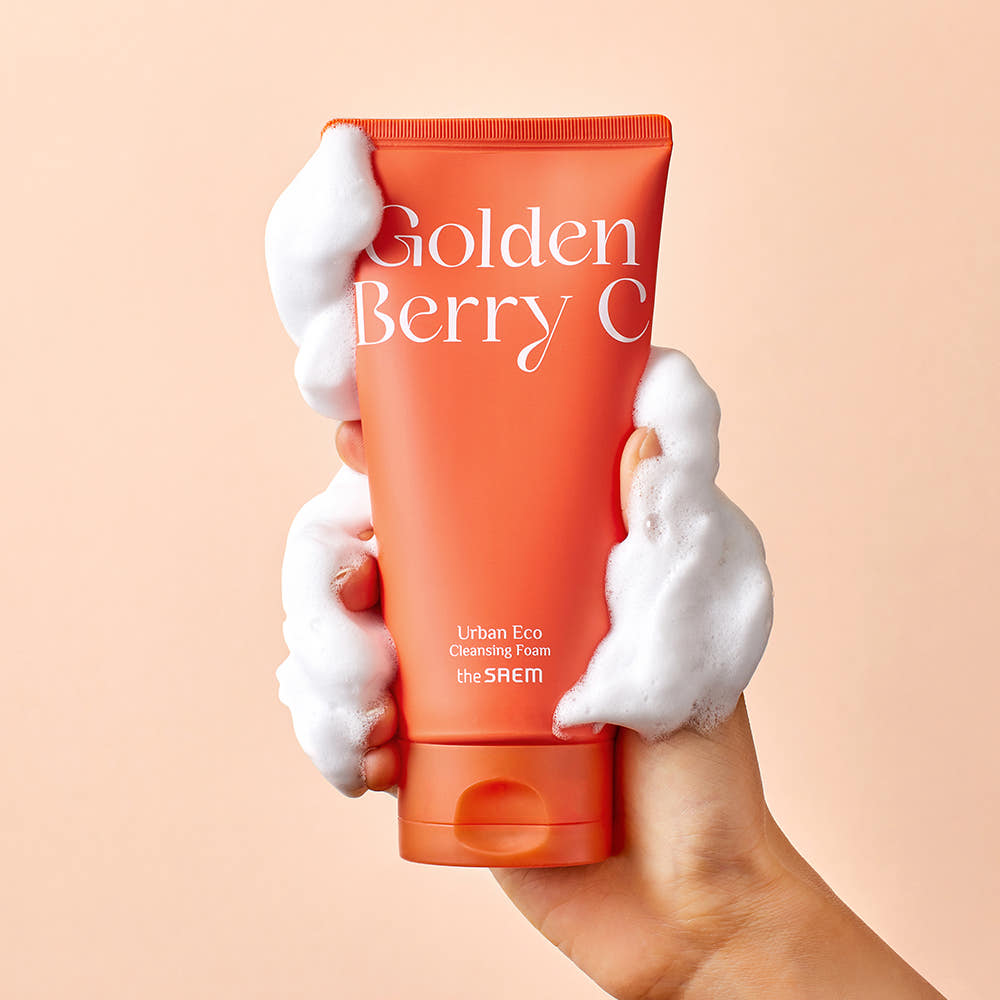 THE SAEM Urban Eco Golden Berry C Cleansing Foam 150ml de la marque, tube orange tenu avec mousse sur fond pastel.