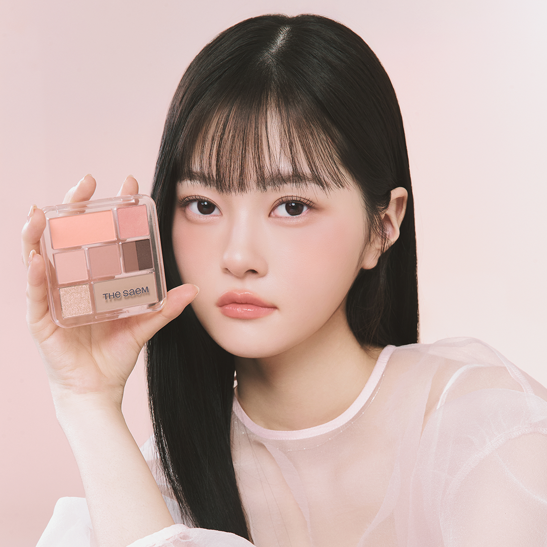 THE SEAM Shadow Box Palette, maquillage dans un décor rose; une femme présente la palette de la marque THE SEAM.