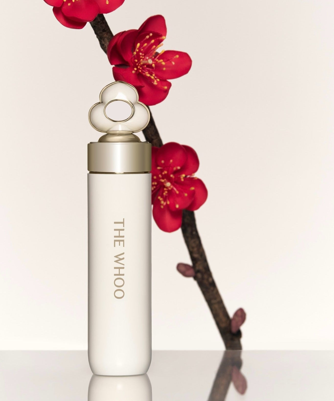 THE WHOO Essentail Lip Glow Balm de la marque THE WHOO, tube blanc posé avec fleurs rouges sur fond clair.
