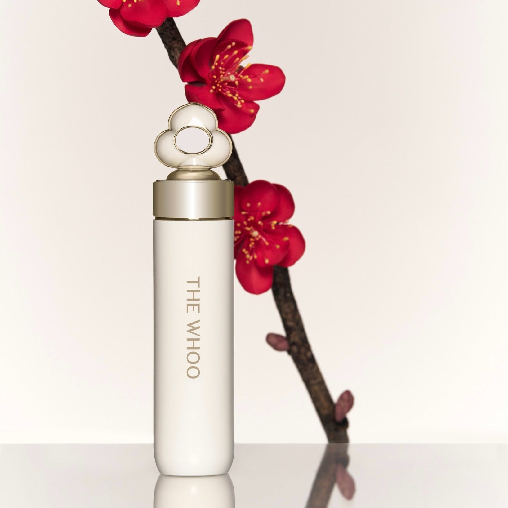 THE WHOO Essentail Lip Glow Balm de la marque THE WHOO, tube blanc posé avec fleurs rouges sur fond clair.