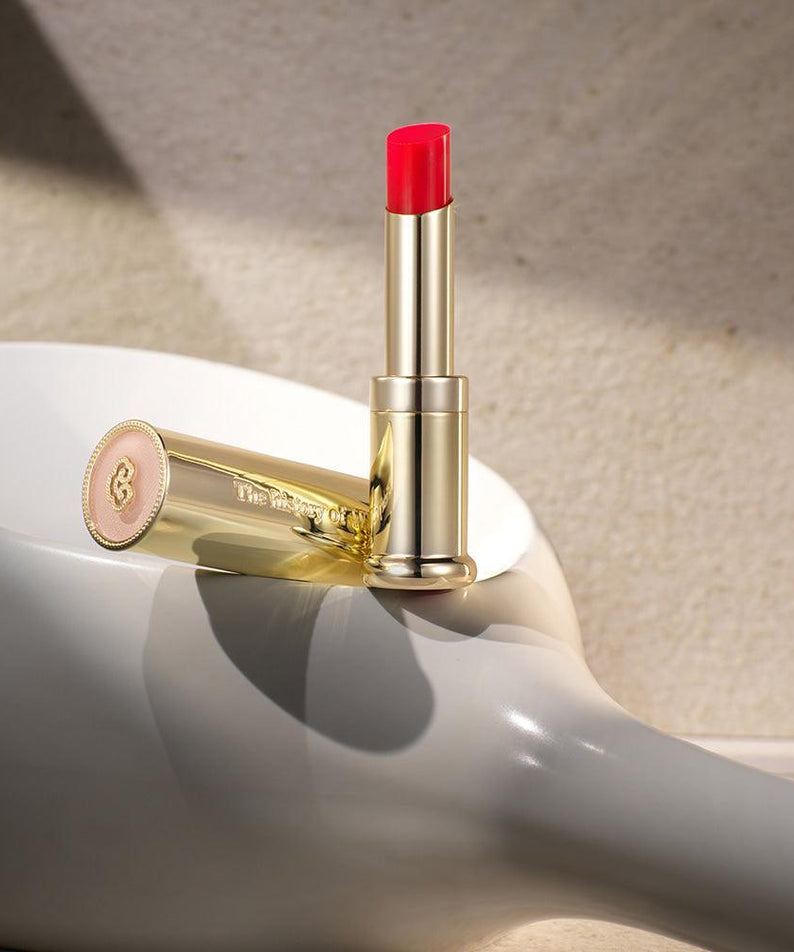 THE WHOO Gong Jin Hyang Mi Glow Lip Balm 3.3g en tube doré sur fond texturé