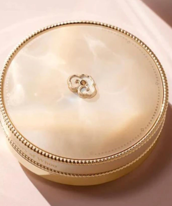 THE WHOO Gong Jin Hyang Mi Luxury Golden Cushion 13g, élégant boîtier doré posé sur une surface rose pâle, lumière douce.