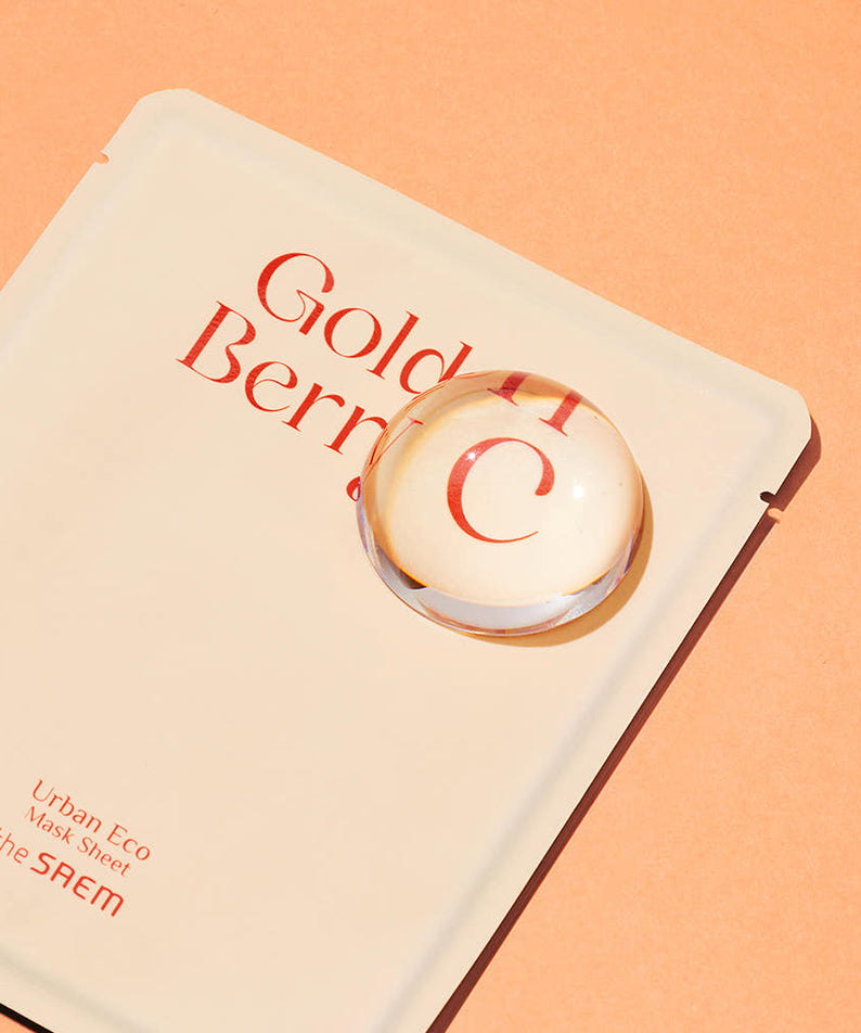 THE SAEM Urban Eco Golden Berry C Mask Sheets 10 Sheets sur fond orange, gros plan d'une feuille de masque et d'une gouttelette.