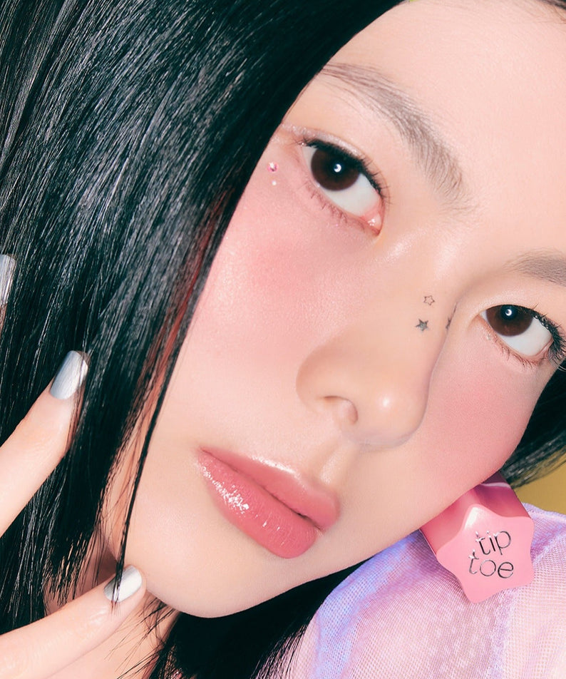 Jeune femme portant TIP TOE Glowit Sorbet Tint avec un maquillage éclatant et des ongles argentés, en gros plan du visage.