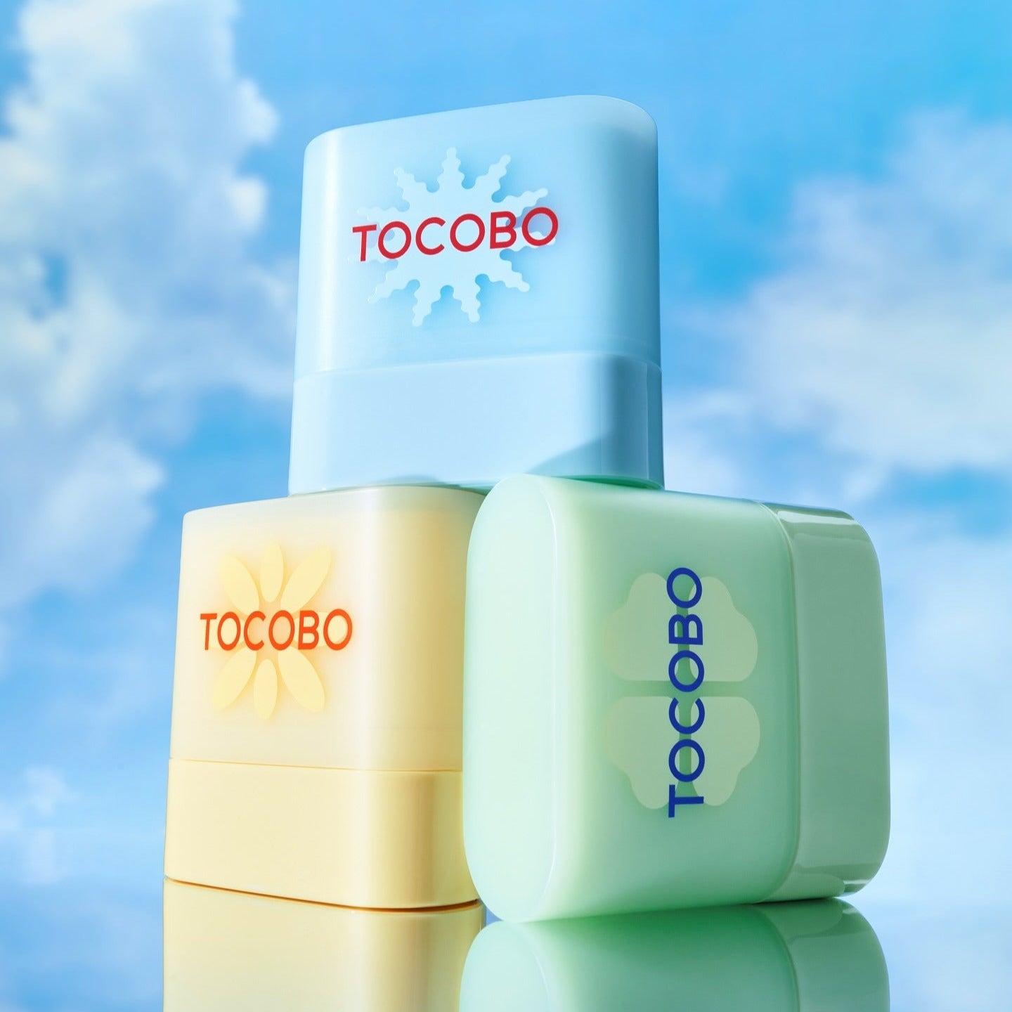 TOCOBO Mini Sun Stick Trio, produits TOCOBO sur fond ciel bleu, prise de vue studio, ambiance estivale