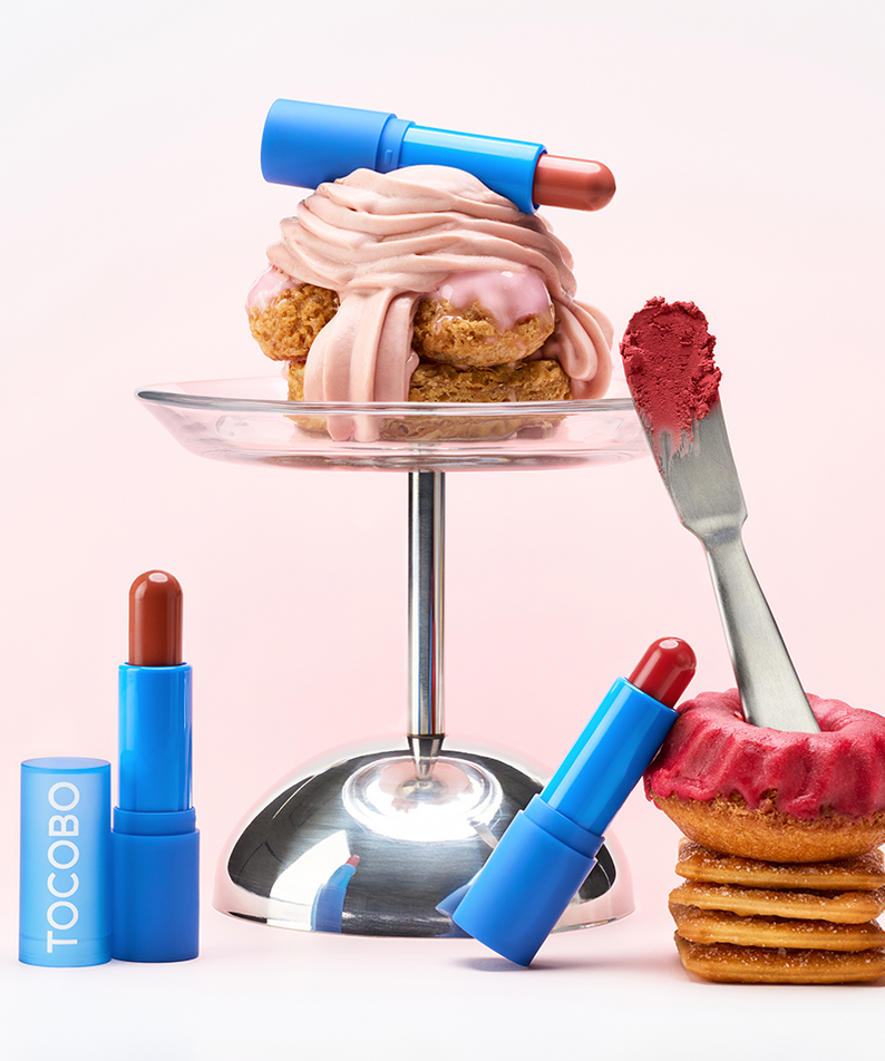 TOCOBO Powder Cream Lip Balm, tube bleu et baume rose sur fond rose, ambiance cosmétique gourmande