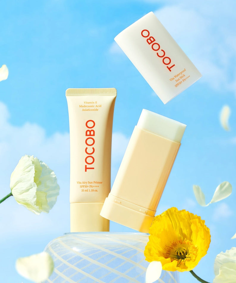 TOCOBO Vita Airy Sun Primer 35ml sur un fond de ciel bleu avec des fleurs blanches et jaunes en décoration, produit de beauté.