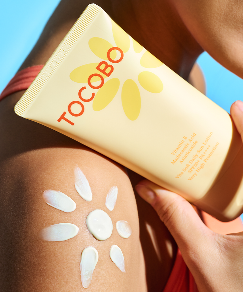 TOCOBO Vita Soft Daily Sun Lotion SPF50+ PA++++ 150ml, tube crème solaire sur peau en plein soleil, fond bleu