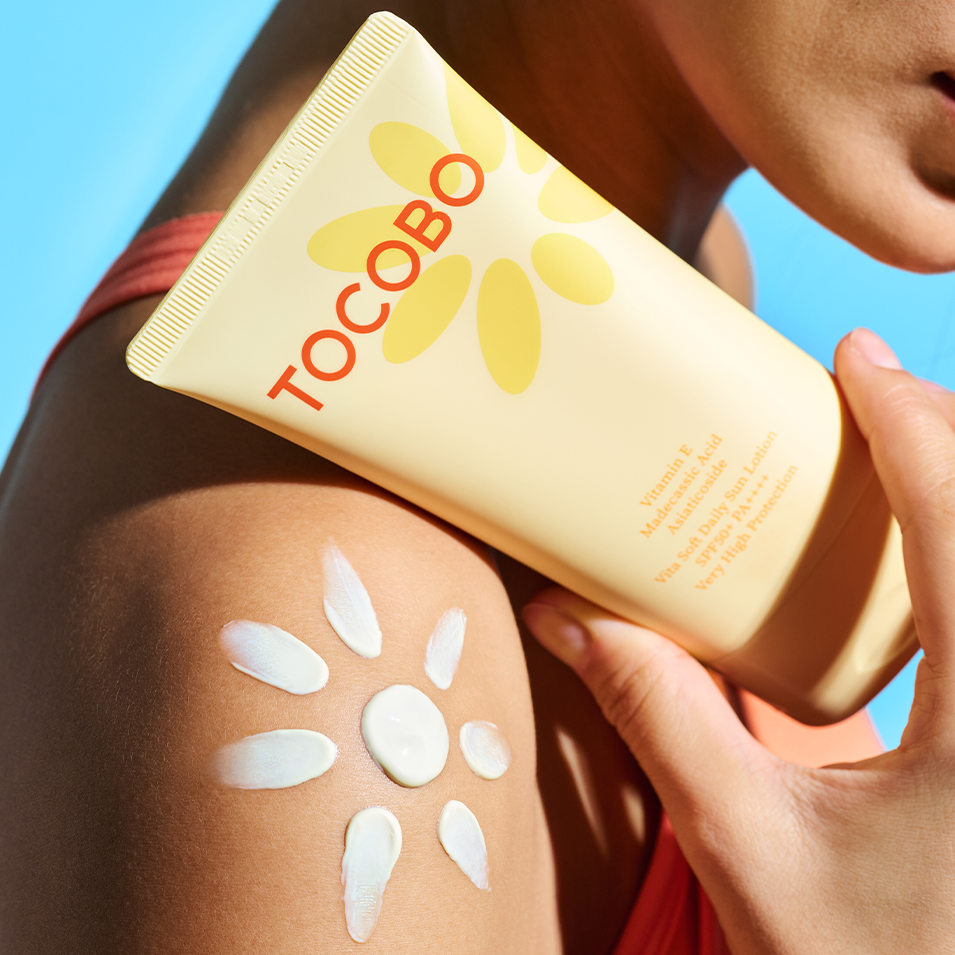TOCOBO Vita Soft Daily Sun Lotion SPF50+ PA++++ 150ml, tube crème solaire sur peau en plein soleil, fond bleu
