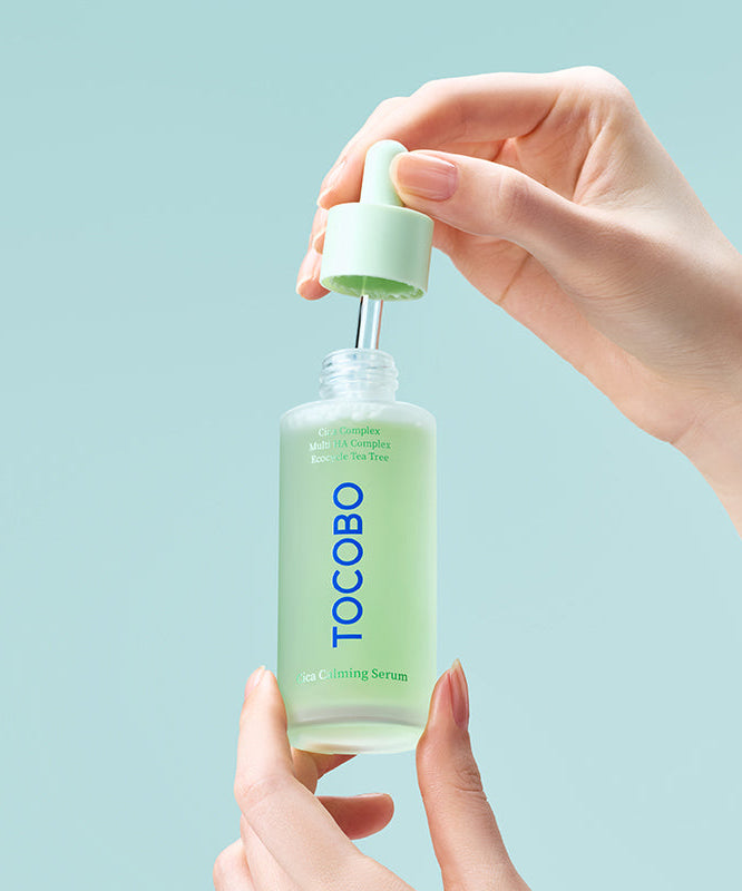 Main tenant TOCOBO Cica Calming Serum, flacon crème Cica, marque TOCOBO sur fond bleu clair, soin apaisant
