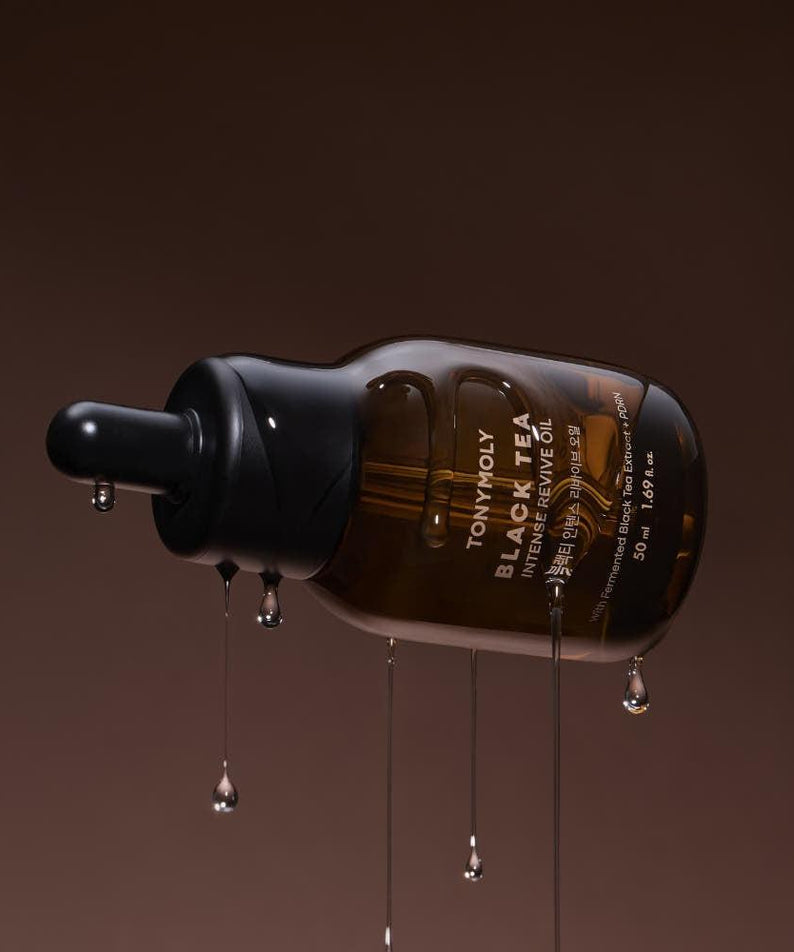 TONY MOLY Black Tea Intense Revive Oil 50ml, flacon noir versé sur fond brun, gouttes et texture huileuse