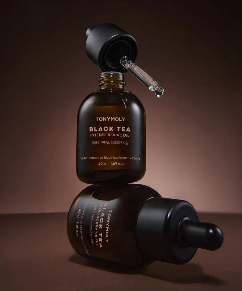 Décris l'image en français : TONY MOLY Black Tea Intense Revive Oil 50ml, flacon et reflet, ambiance sombre.